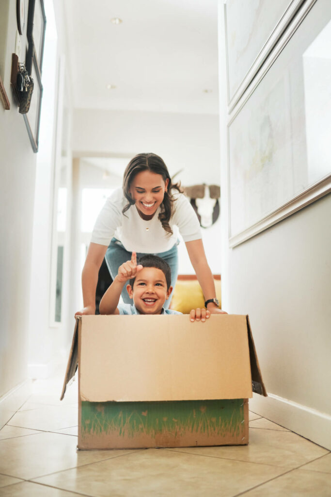 Mum pushing child in box, laughing.