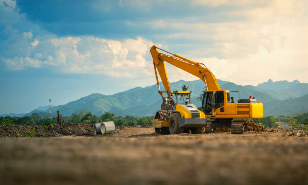 Digger and roller on rural construction site.